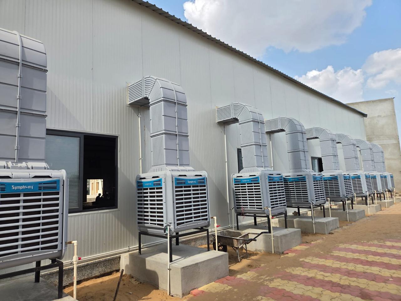 A row of Symphony industrial air coolers with vertical GI ducting along a factory building.