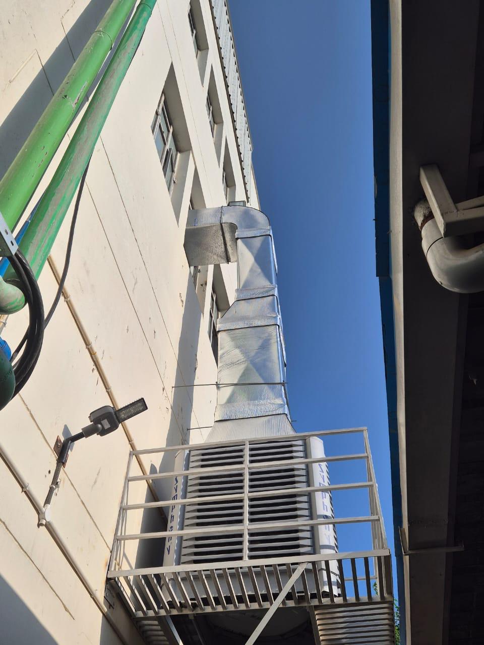 Bracket-mounted air cooler with a vertical GI duct rising along a building wall.
